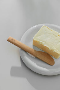 Block of butter placed on a small white plate alongside small wooden butter knife