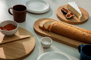 Breakfast table with a pate in a small bowl, baguette, brie cheese, pieces of fig all placed on the wooden cutting boards of different sizes