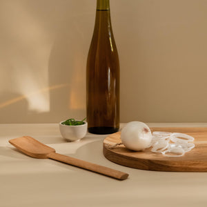 Kitchen counter with simple wooden spatula, white onion cut and placed on the wooden cutting board, brown bottle and some herbs in the small bowl