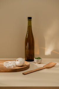 Wooden standard spatula placed by the cutting board with white onion cut in slices, brown glass bottle, and small bowl with rosemary