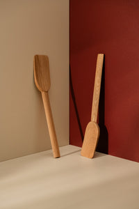 Two simple wooden spatulas leaning against beige and red walls
