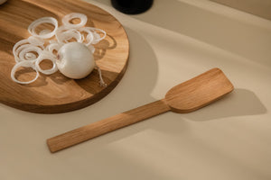 Simple wooden spatula placed alongside wooden cutting board with some white onion pieces