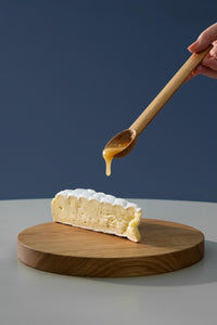 Woman dripping honey from a small wooden spoon on a brie cheese placed on a round wooden cutting board