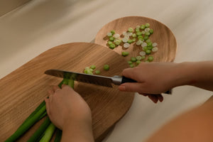 Woman cutting spring onion on a wooden cutting board and setting aside already cut pieces on the round plate-like cutting board