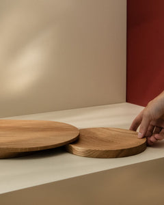 Small round wooden plate-like cutting board being placed under a larger one to show functionality of a set