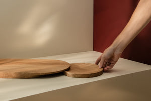 Small round wooden plate-like cutting board being placed under a larger one to show functionality of a set