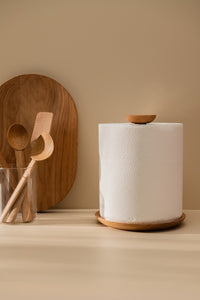 Large paper towel roll in a wooden holder placed on a kitchen counter alongside wooden kitchen utensils and a cutting board