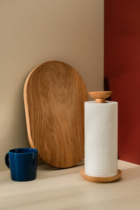 Small paper towel roll in a holder placed on a kitchen counter alongside wooden cutting board and navy cup