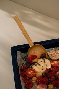Shovel-like wooden spatula placed in a baking tray with roasted tomatoes and garlic