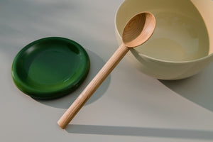 Large wooden spoon leaning on a large yellow bowl placed besides small green plate