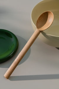Large wooden spoon leaning on a large yellow bowl placed besides small green plate